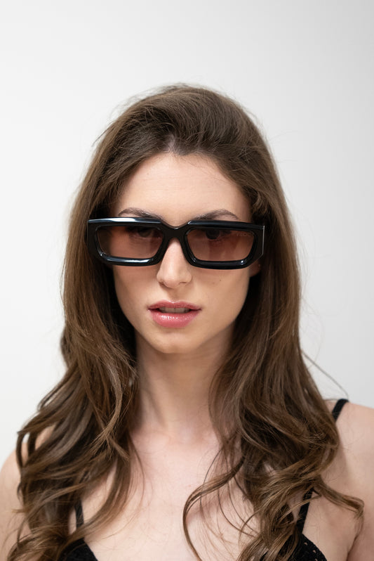 femme qui porte Lunettes de soleil noires à la monture épaisse et affirmée de la marque VROC. 